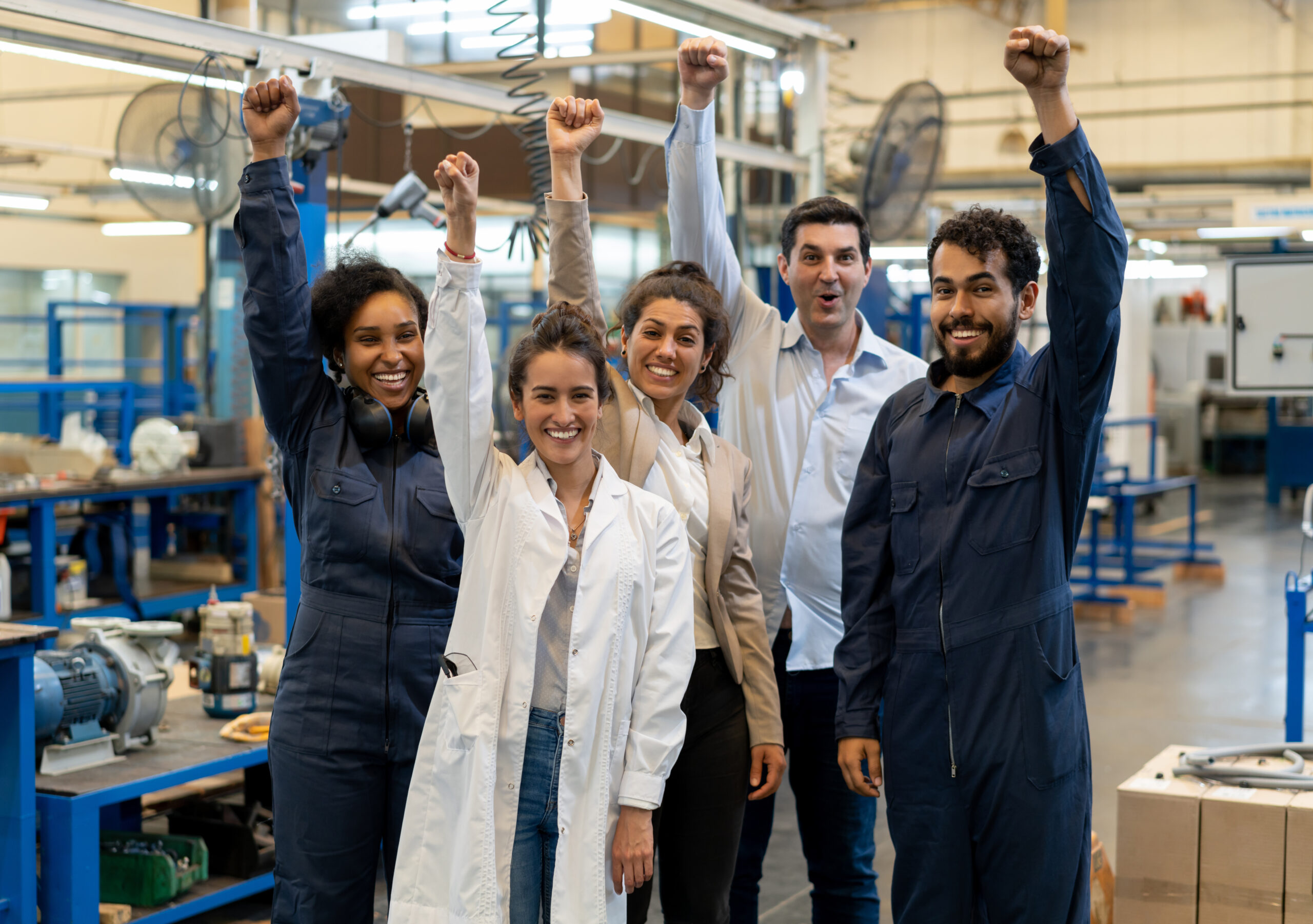 Multi Ethnic Team Of Employees At A Manufacturing Water Pump Factory With Hands Up Smiling At Camera